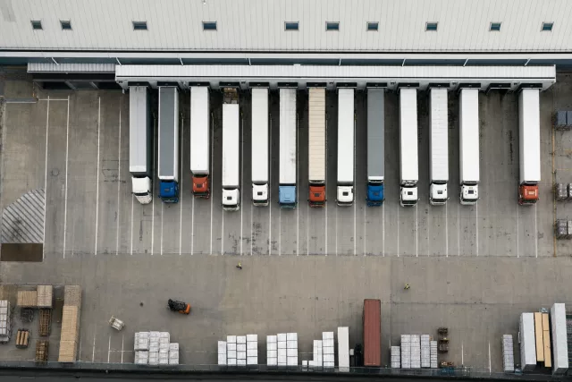 Vue aérienne verticale d’une cour de chargement avec camions reculés à quai, palettes et chariots élévateurs, illustrant la mesure des KPI transport et la performance logistique.