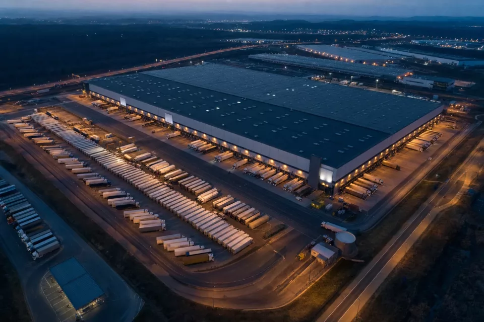 Vue aérienne au crépuscule d’un grand hub logistique avec semi-remorques alignés aux quais, illustrant la coordination des approvisionnements collaboratifs VMI, SMI et GPA.