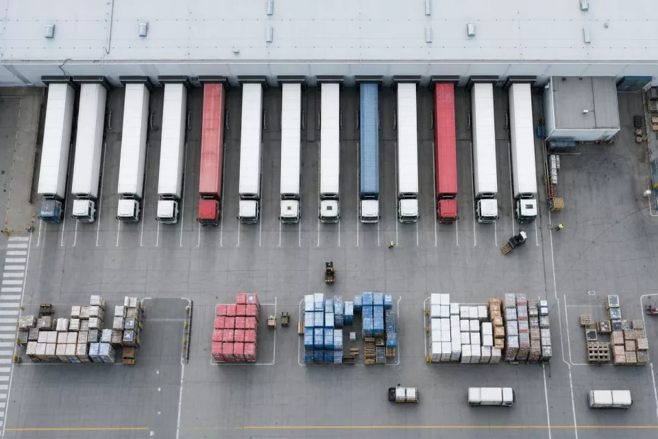 Vue aérienne verticale d’une cour de chargement logistique avec camions à quai et palettes, illustrant un WMS 3PL pour des opérations multi-clients et l’onboarding EDI.