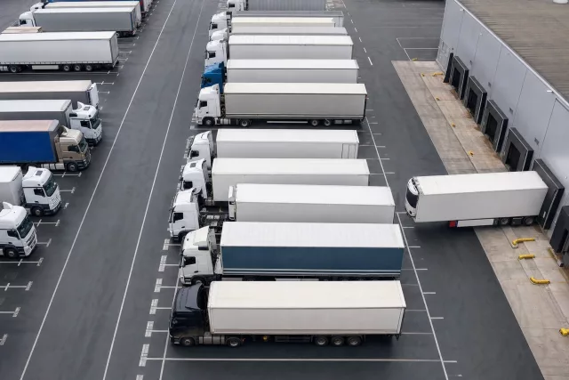 Vue aérienne éditoriale d’une flotte de poids lourds stationnés en cour, en trame régulière, illustrant un YMS pour fluidifier la gestion des quais et des flux logistiques.