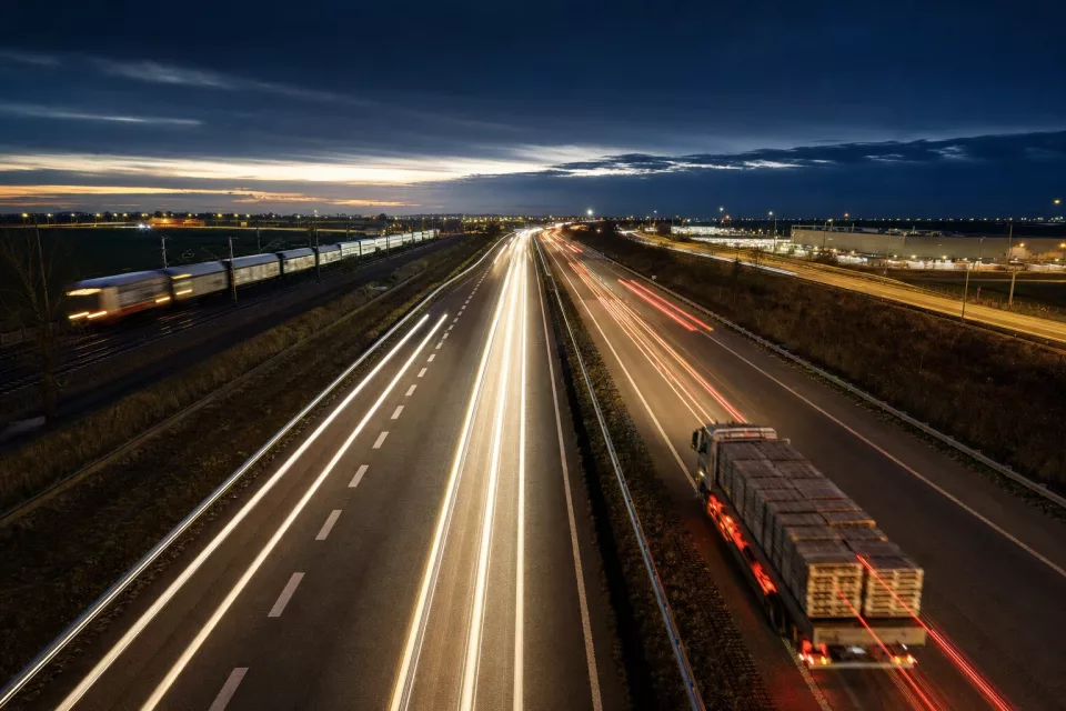 Autoroute logistique de nuit vue depuis un pont, avec les traînées lumineuses des poids lourds, illustrant un appel d’offres transport fondé sur la comparaison des performances et des coûts.