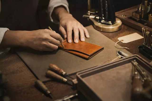 Gros plan éditorial d’un atelier de personnalisation en magasin, avec les mains d’un artisan sur un article en cuir, illustrant un commerce unifié reliant expérience client et exécution.