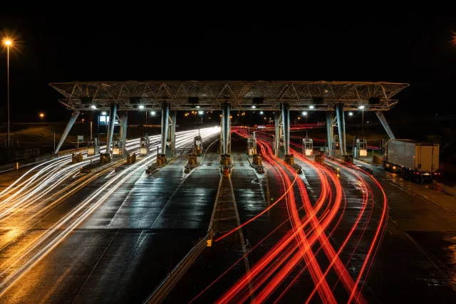 Photo en pose longue d’un péage autoroutier de nuit, avec des traînées lumineuses de véhicules et un camion en attente, évoquant le temps d’attente camion quai et le coût de l’immobilisation.
