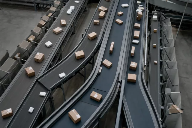Vue en plongée d’un réseau de convoyeurs où des colis suivent des flux divergents, illustrant l’orchestration des commandes et l’arbitrage du stock.