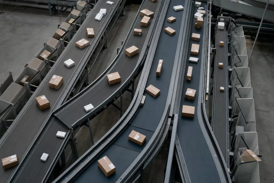 Vue en plongée d’un réseau de convoyeurs où des colis suivent des flux divergents, illustrant l’orchestration des commandes et l’arbitrage du stock.