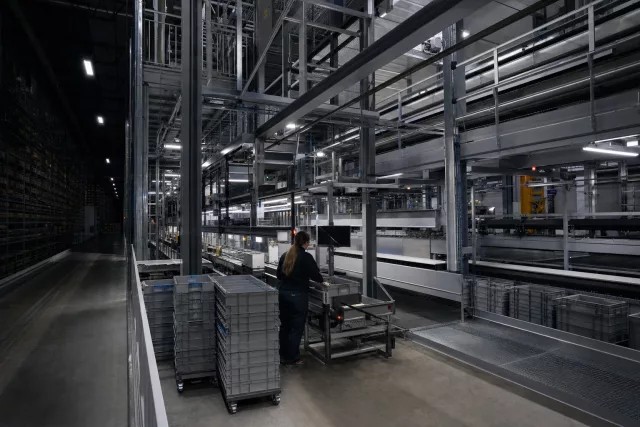 Vue nocturne d’une mezzanine automatisée de préparation de commandes avec un opérateur et des bacs navette, illustrant un tableau de bord entrepôt piloté par les données WMS.