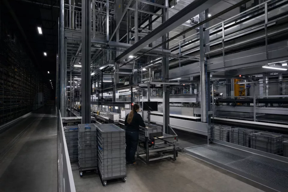 Vue nocturne d’une mezzanine automatisée de préparation de commandes avec un opérateur et des bacs navette, illustrant un tableau de bord entrepôt piloté par les données WMS.