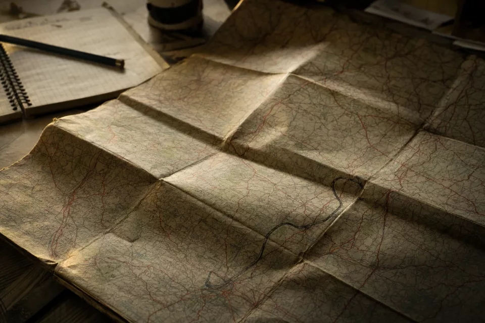 Macro d’un atlas routier plié et usé, avec un tracé au crayon vers une cour logistique, illustrant le dimensionnement des places et la planification des flux de camions.