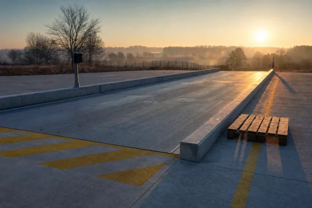 Pont-bascule en acier vide à l’aube, avec une palette Europe posée à côté de la plateforme, évoquant le contrôle et le rapprochement d’un compte palettes.